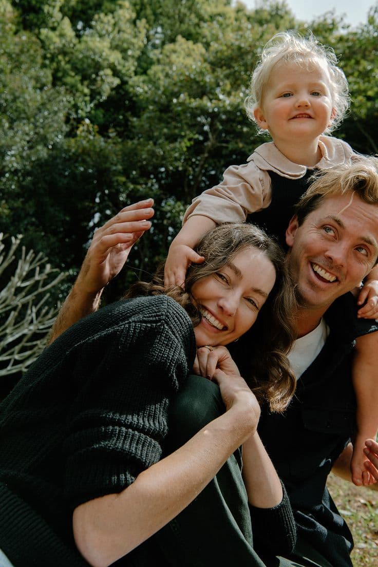 Family smiling together outdoors with child on shoulders